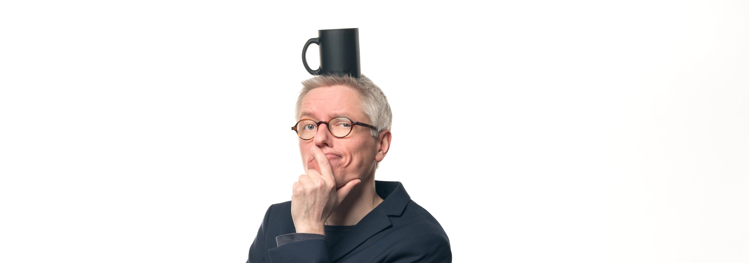 Dr. Bartholomäus Winkler balanciert eine schwarze Werbetasse auf dem Kopf